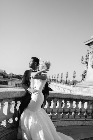 A romantic black and white photo of a couple embracing on an ornate balcony with classical architecture.
