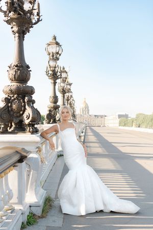 Bride in flowing white gown poses on ornate bridge with decorative lampposts in Paris.