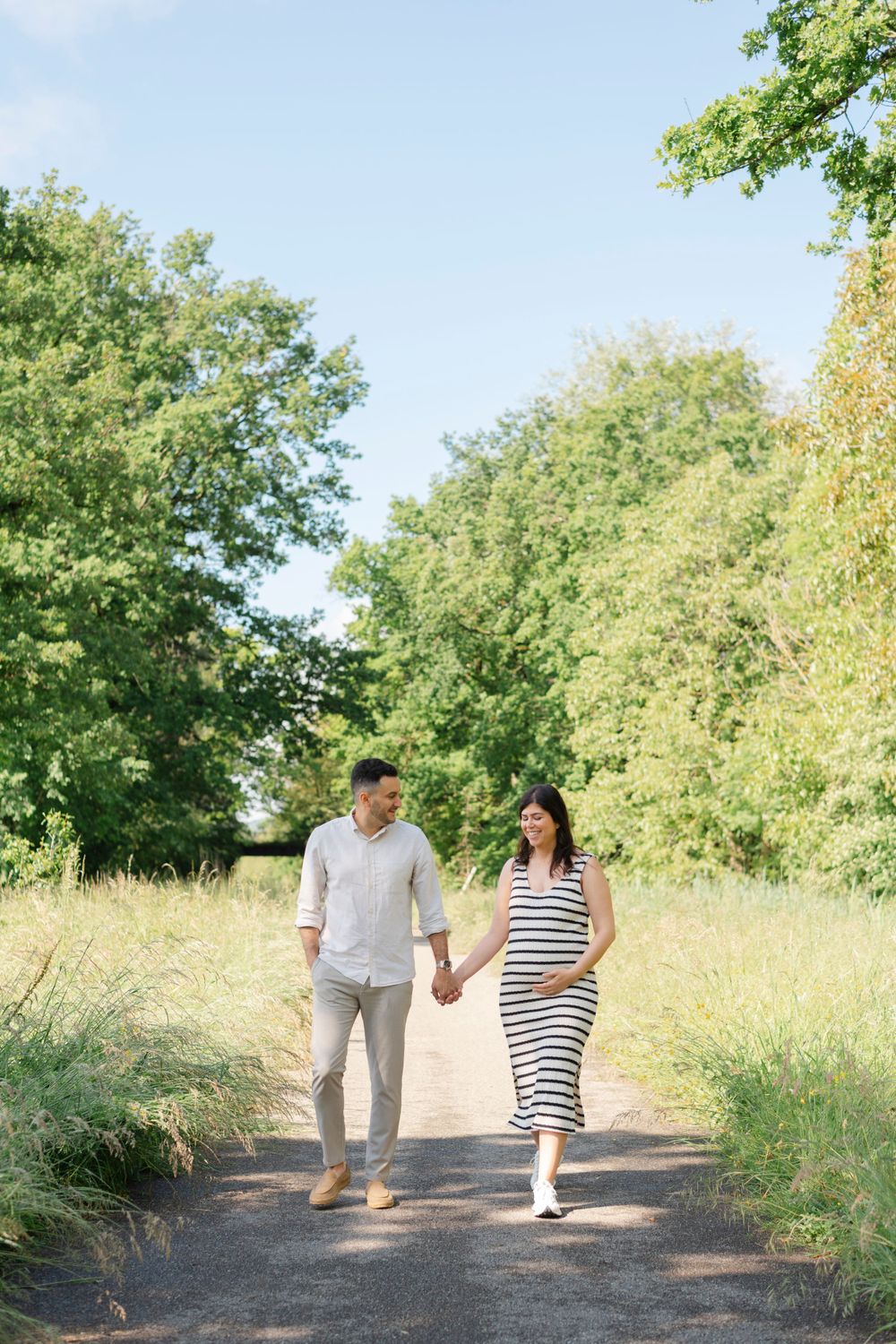 Couple walking hand in hand on sunny nature path surrounded by green trees.