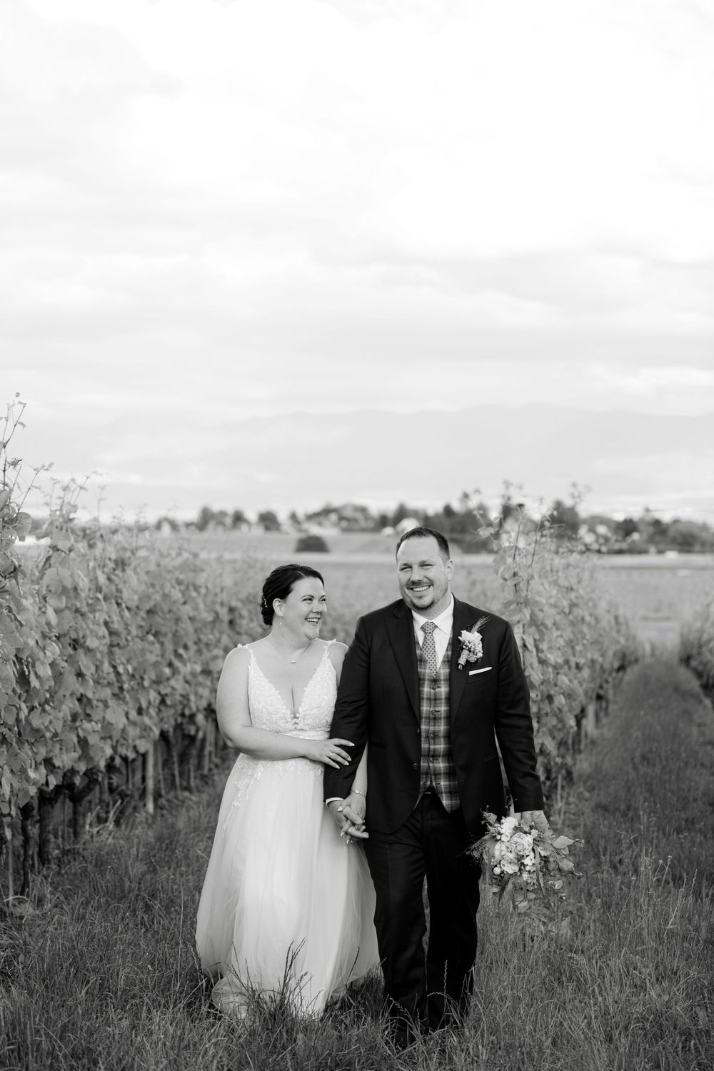 Black and white portrait of newlyweds walking together through a vineyard.