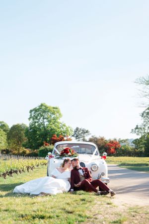 Wedding couple resting by vintage white car decorated with flowers on countryside road.