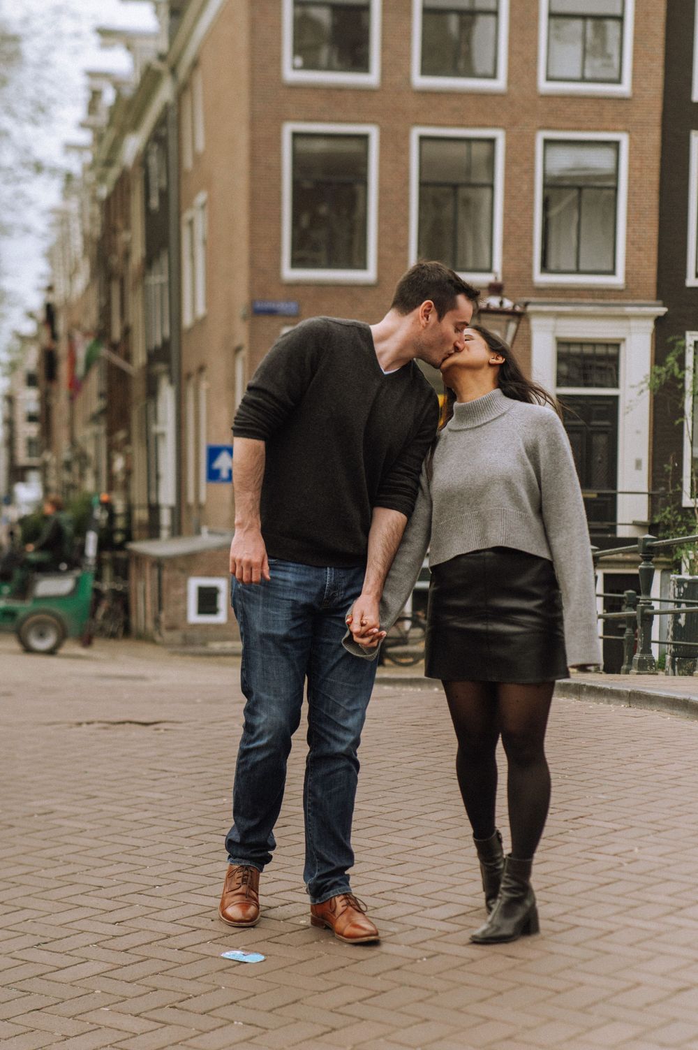 A couple walks hand in hand along a cobblestone street in Amsterdam.