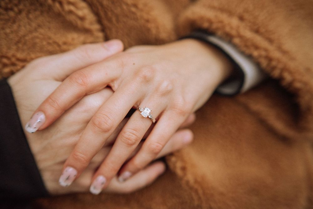 Close-up of hands showing off an engagement ring against a fuzzy brown coat.