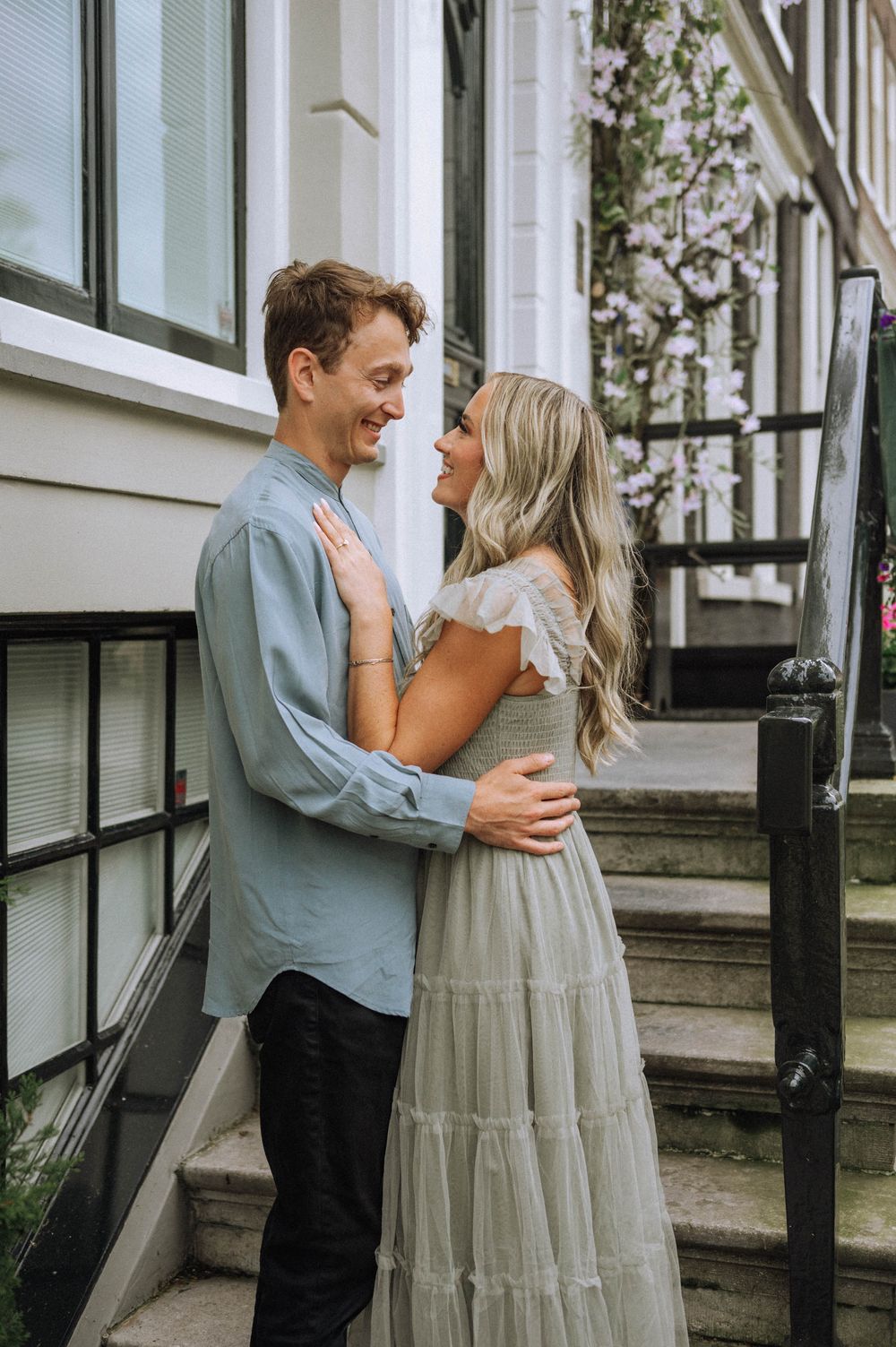 A romantic moment between a couple on stone steps with white windows in the background.