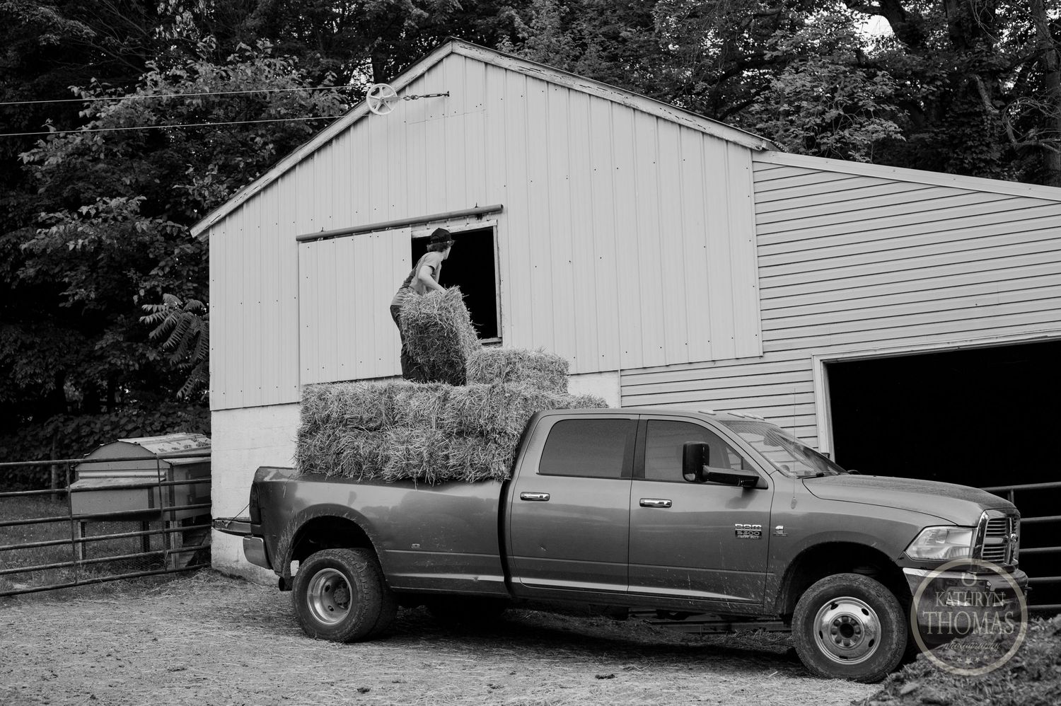 Gray pickup truck loaded with hay bales parked next to a white barn.