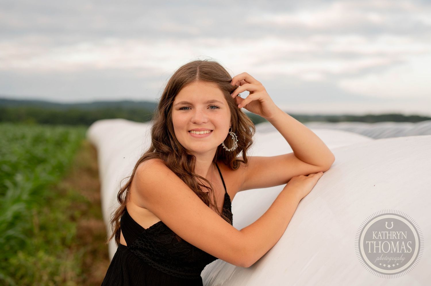 Person leans against a round hay bale in a summer field during golden hour.