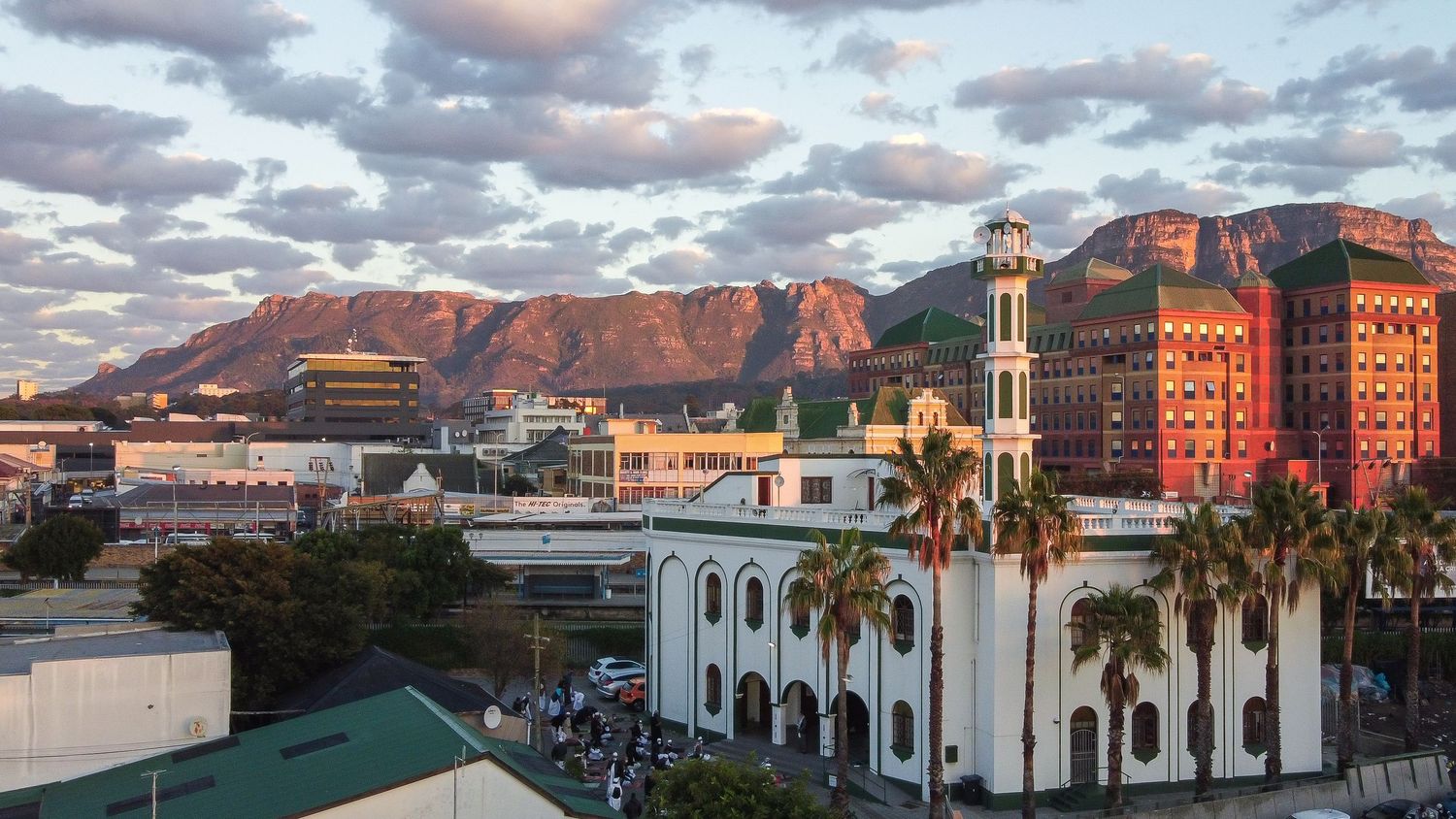 A mosque with white minarets sits against a backdrop of red mountains in Cape Town.