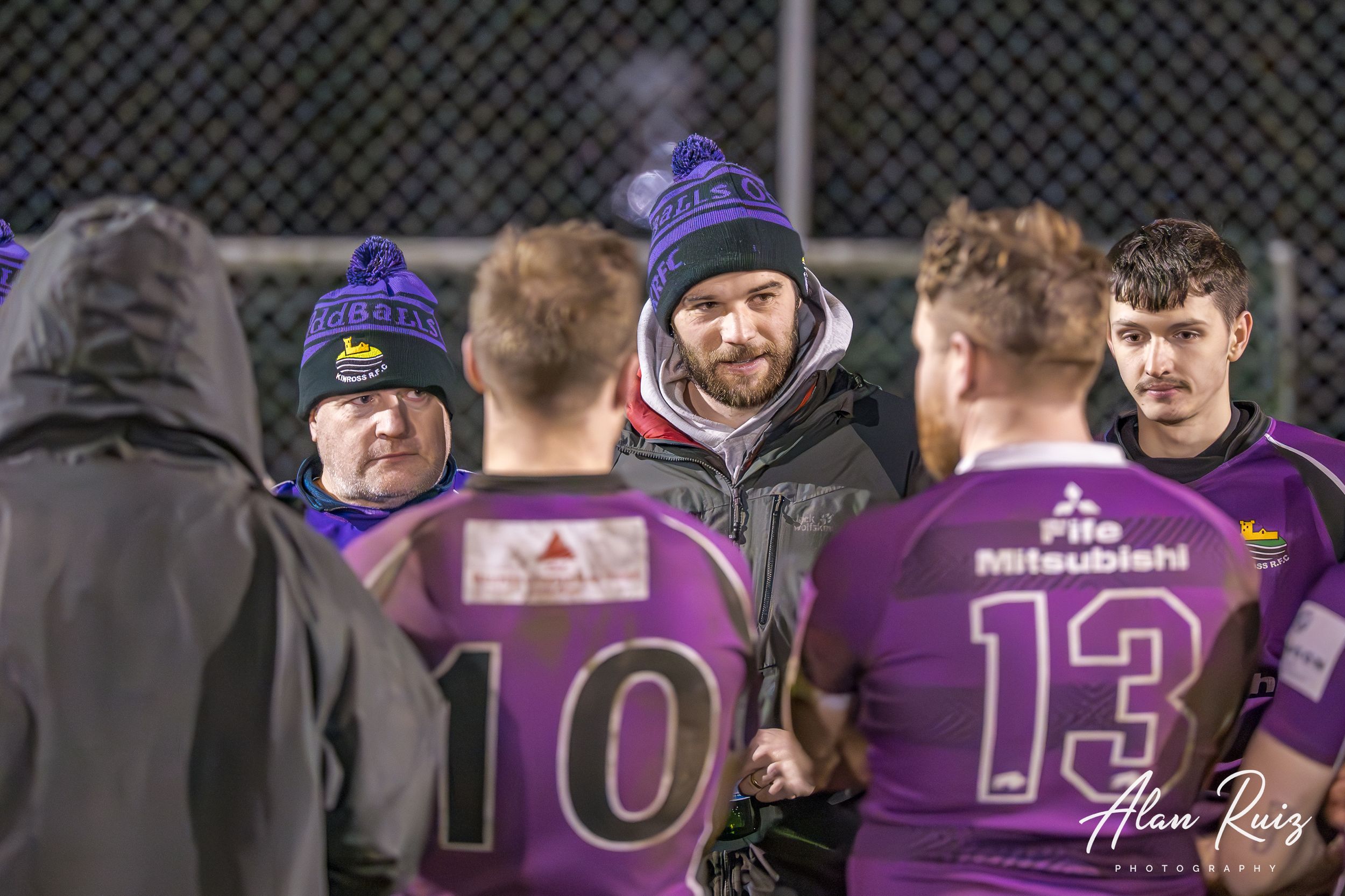 Rugby players in purple jerseys form a sideline lineup during a nighttime match.