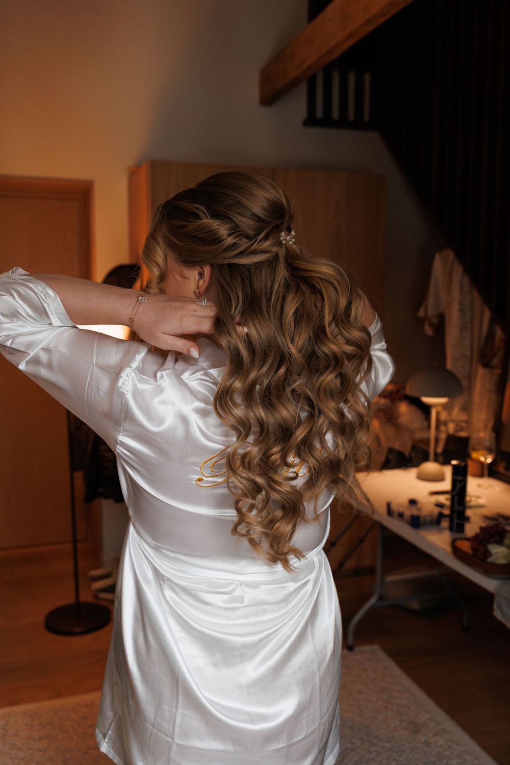 Long wavy brown hair styled elegantly on person wearing white silk robe during wedding preparations.