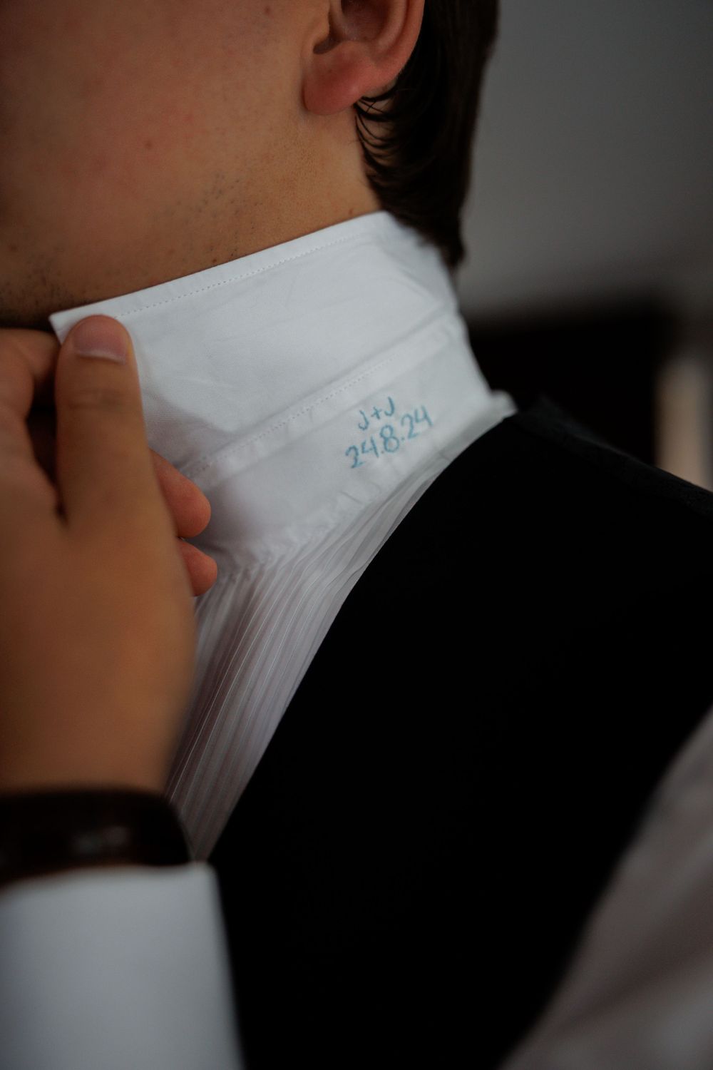 Close up detail of someone adjusting a crisp white dress shirt collar with blue embroidered details.