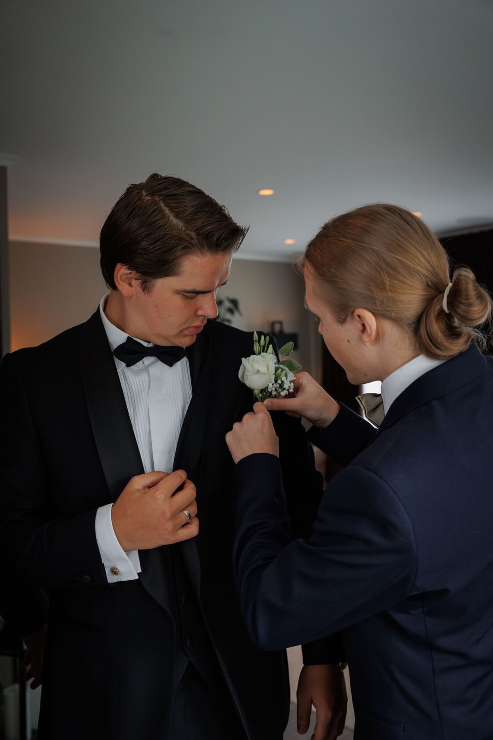 A white boutonniere is being pinned onto a formal tuxedo at an elegant event.