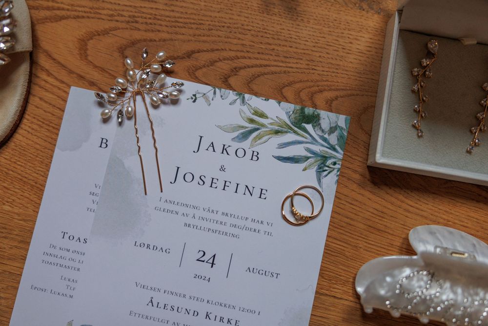 Wedding invitation card with floral design and gold rings laying on wooden surface with decorative elements.