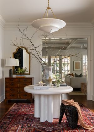 Elegant foyer with white pedestal table, modern pendant light, and vintage oriental rug beneath dried branch arrangement.