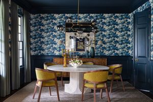 Navy blue floral wallpaper adorns the walls of an eclectic dining room with yellow velvet chairs and modern decor.