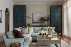 A modern living room features teal shutters, light blue sofas, and soft natural lighting through sheer curtains.