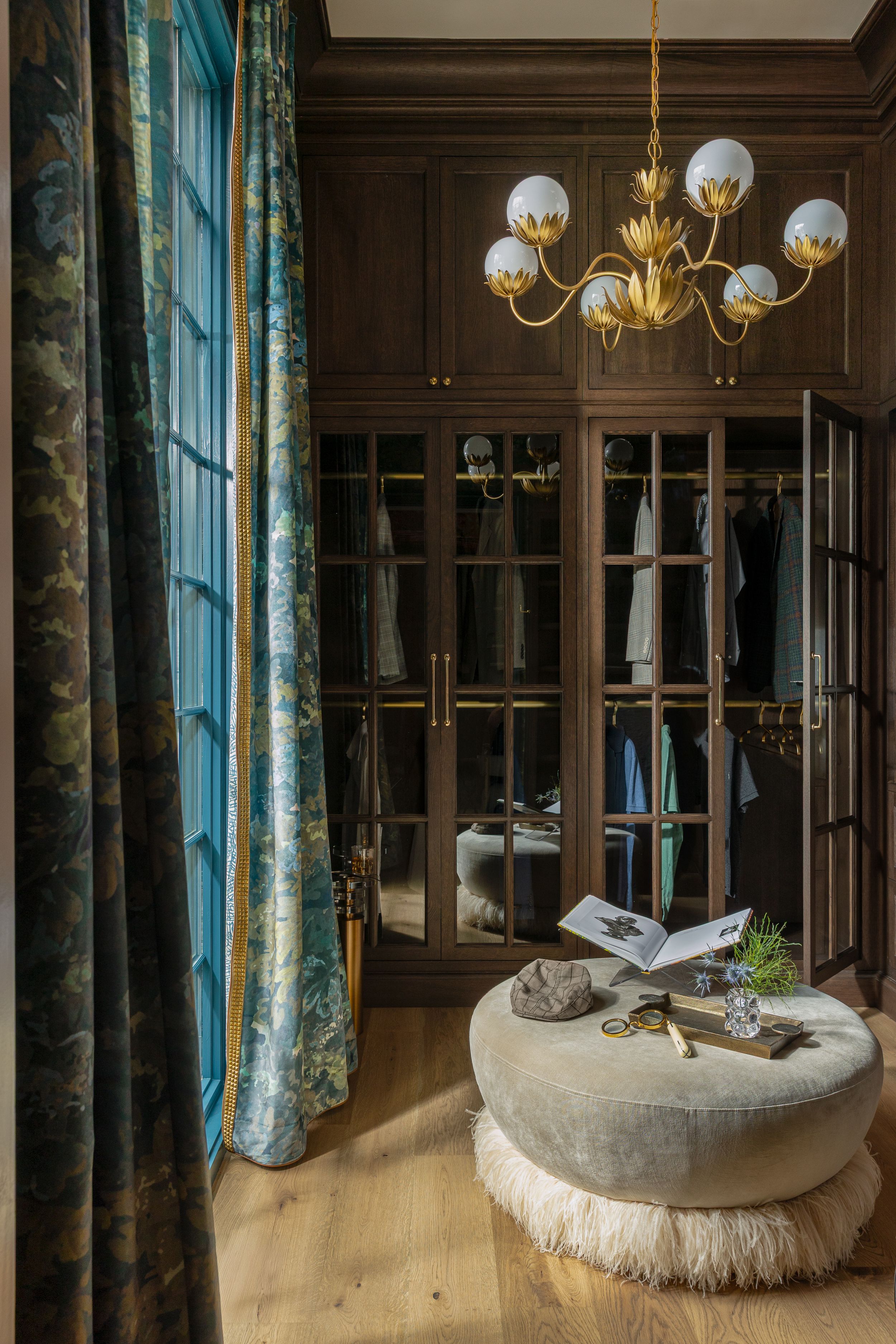 Luxurious hanging papasan chair suspended from ceiling in elegant room with brass chandeliers and large windows.