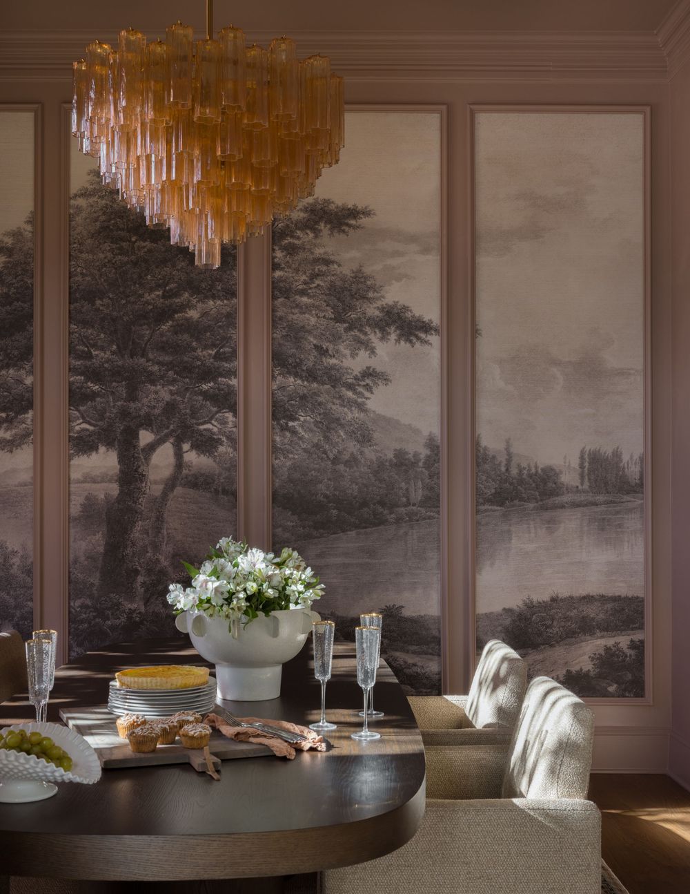 Elegant dining room with scenic mural wallpaper, amber chandelier, oval dark wood table, and white floral centerpiece.