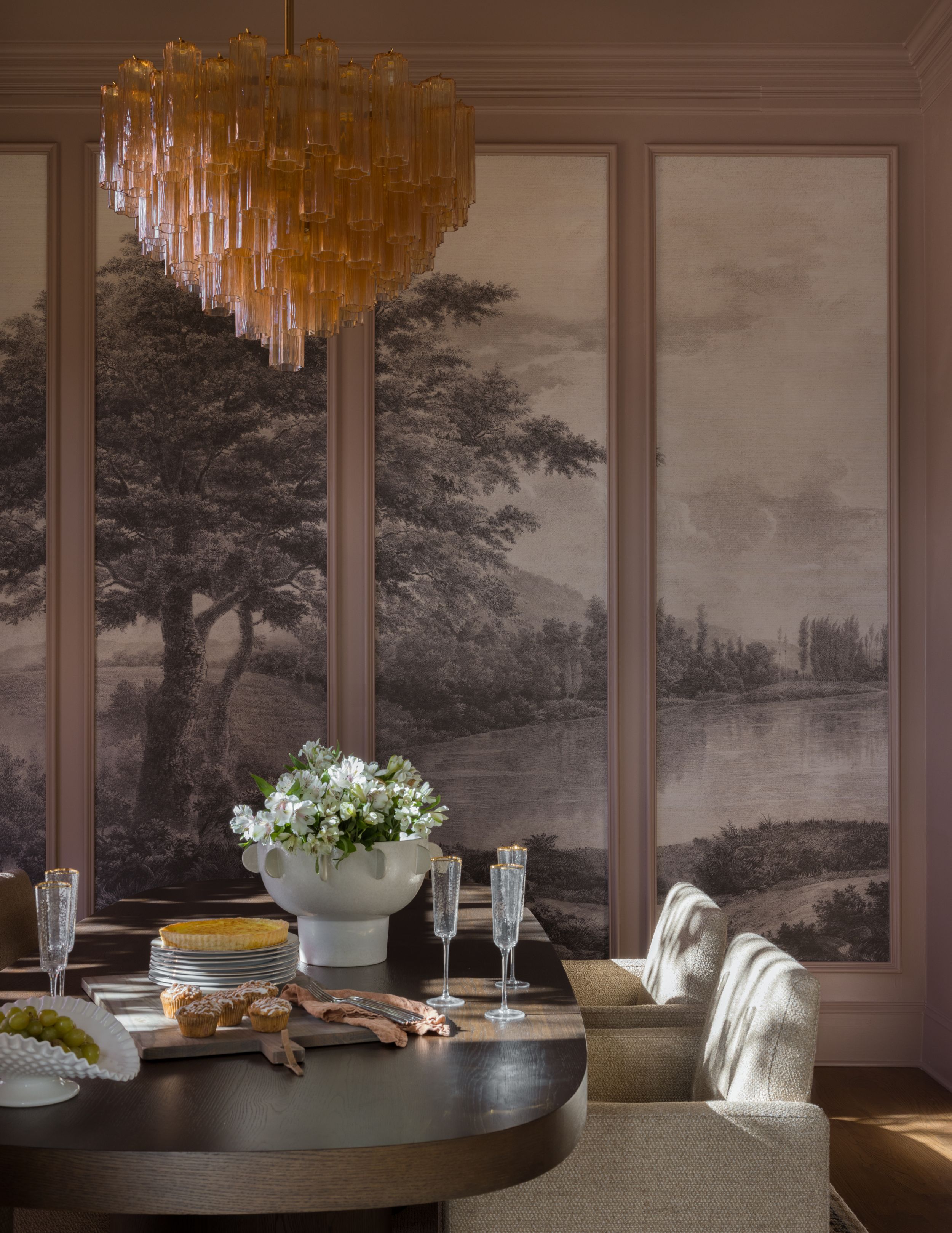 Elegant dining room with scenic mural wallpaper, amber chandelier, oval dark wood table, and white floral centerpiece.