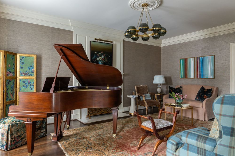 A modern living room features light gray wallpaper, crown molding, and a brass spherical chandelier.