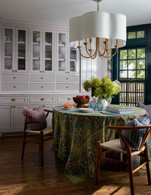 Elegant dining room with round table, colorful tablecloth, wishbone chairs, white built-in cabinetry, and large drum chandelier.