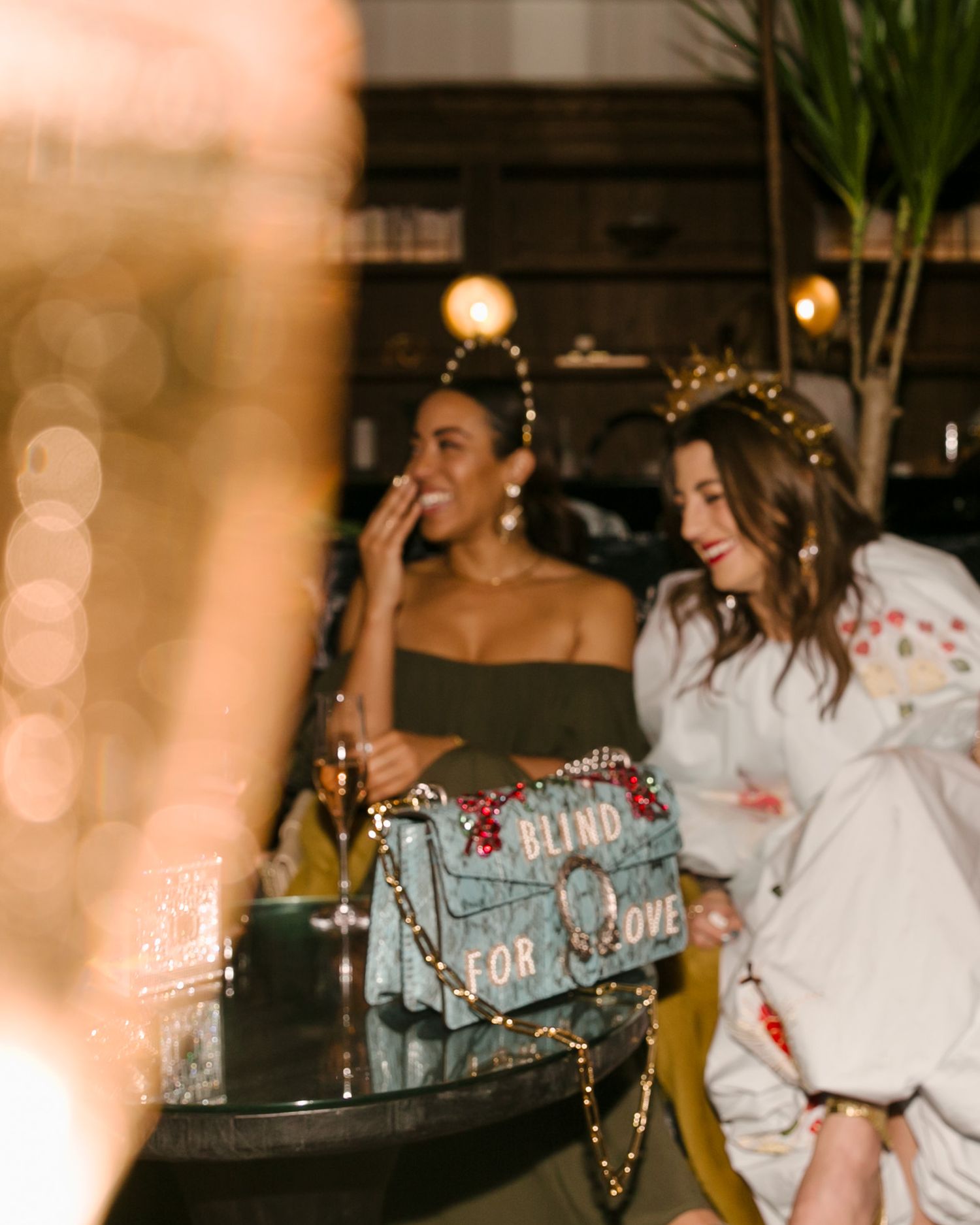 Two friends celebrating at a party with glowing fairy lights and decorative crowns in a dimly lit venue.
