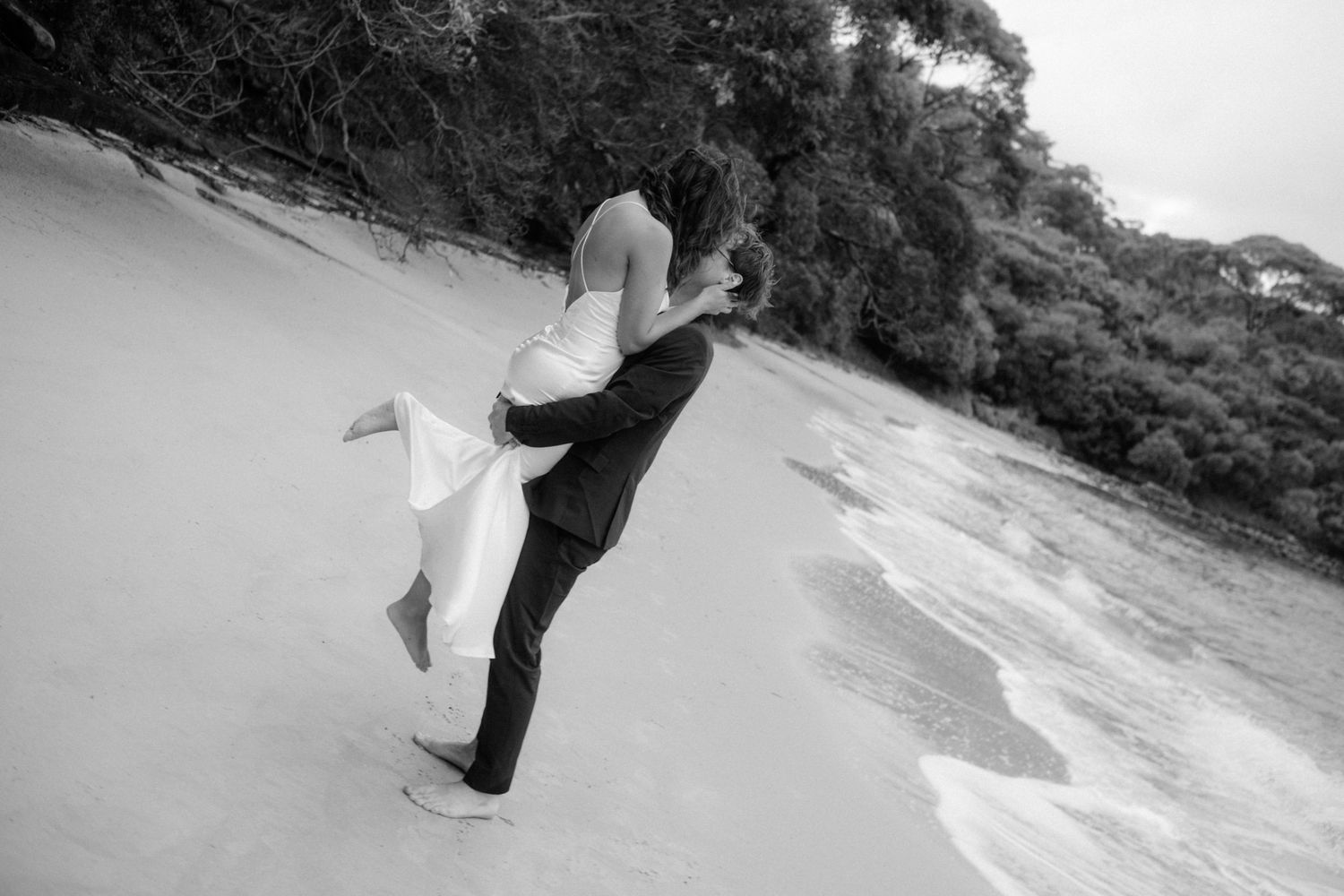 A couple dancing on a black sand beach with flowing dress and long hair caught in the wind at sunset.