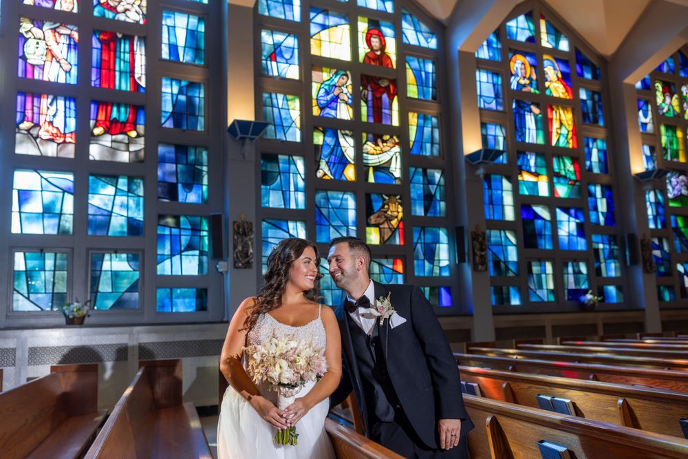 Bride and groom sharing an intimate moment in a church aisle surrounded by stunning colorful stained glass windows.