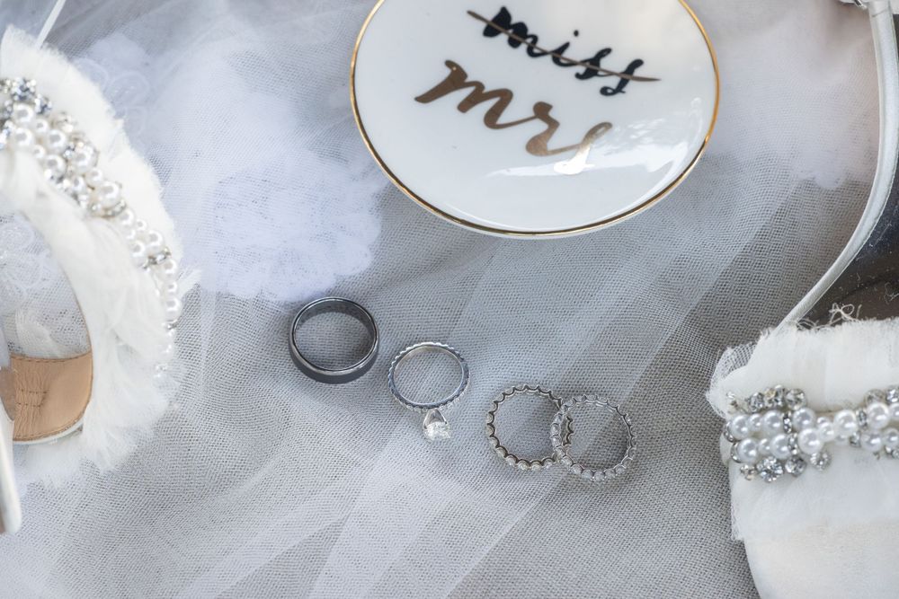 Wedding rings and bands displayed on white tulle next to a miss mr ring dish and bridal accessories.