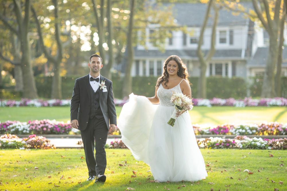 Bride and groom walking through lush garden grounds with colorful flower beds at golden hour.