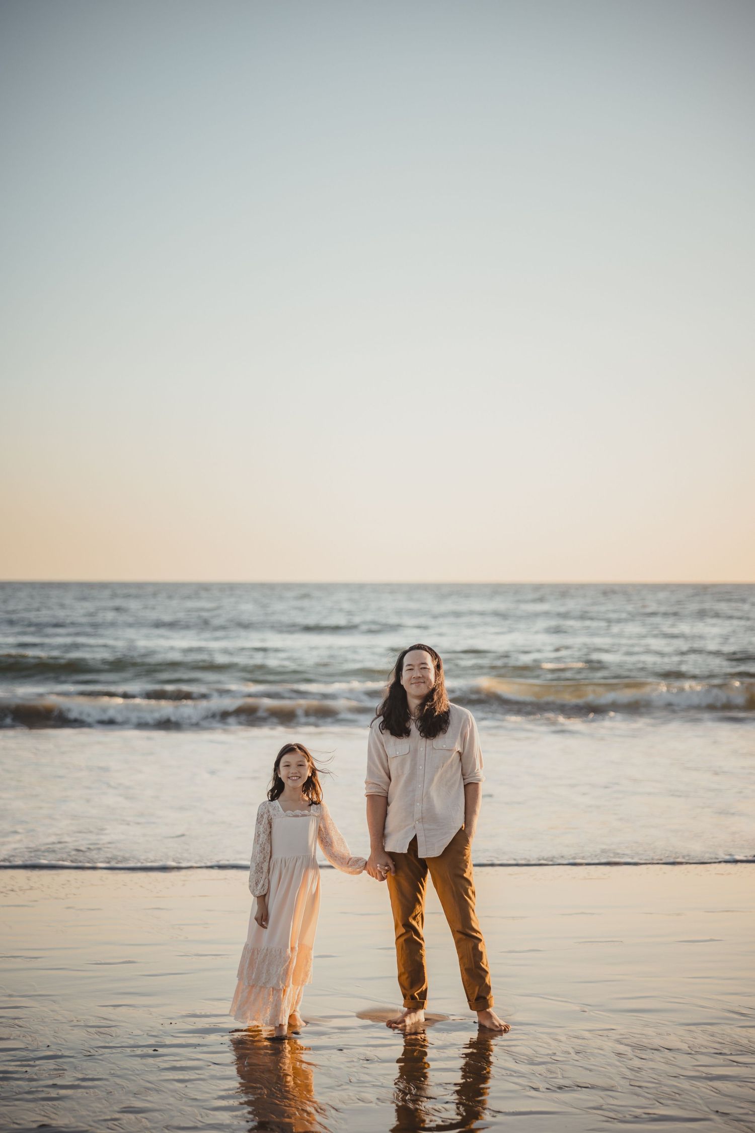 Two people holding hands while standing in shallow ocean water at sunset on a peaceful beach.