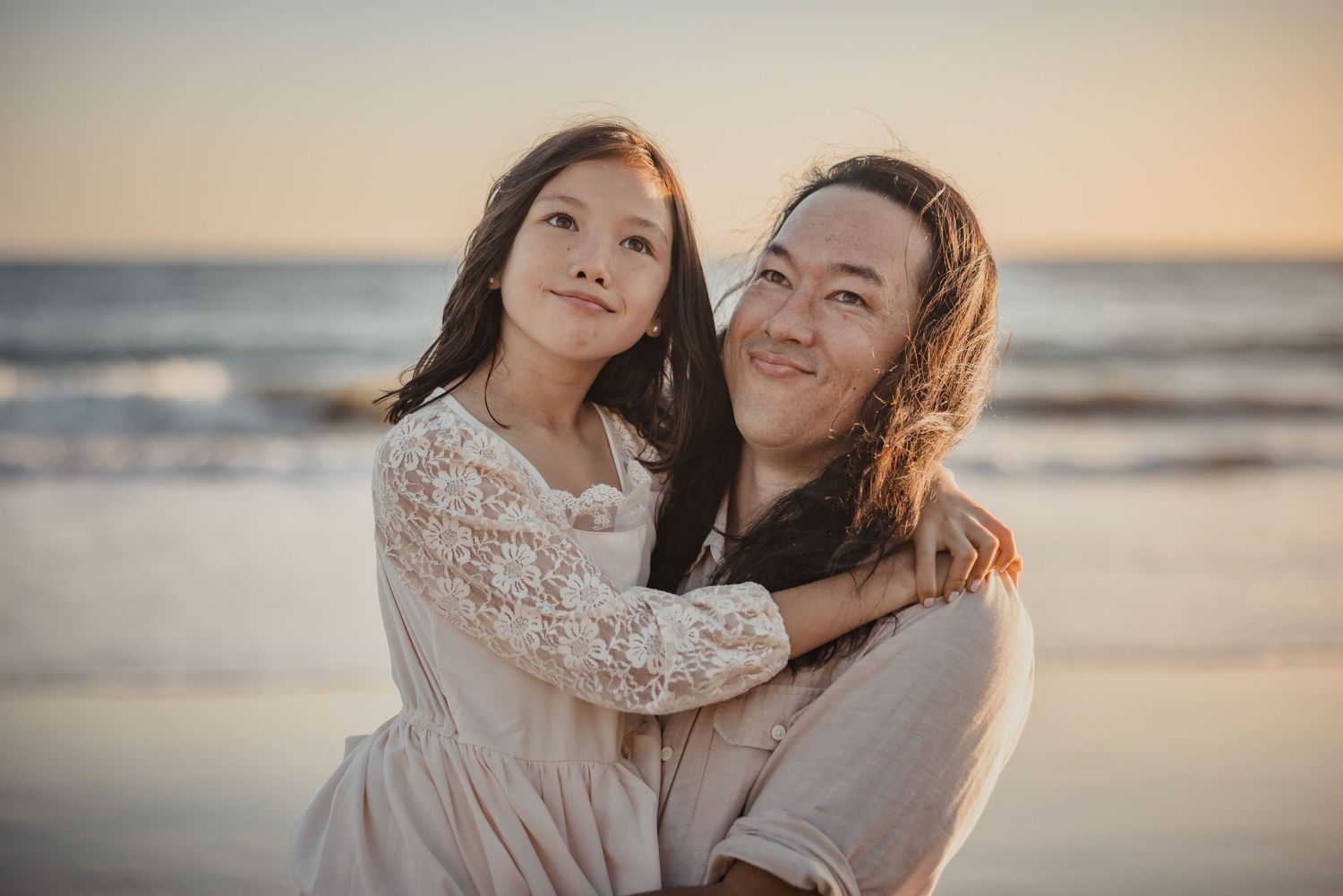 Two people embracing while smiling at sunset on a beach with ocean waves in the background.