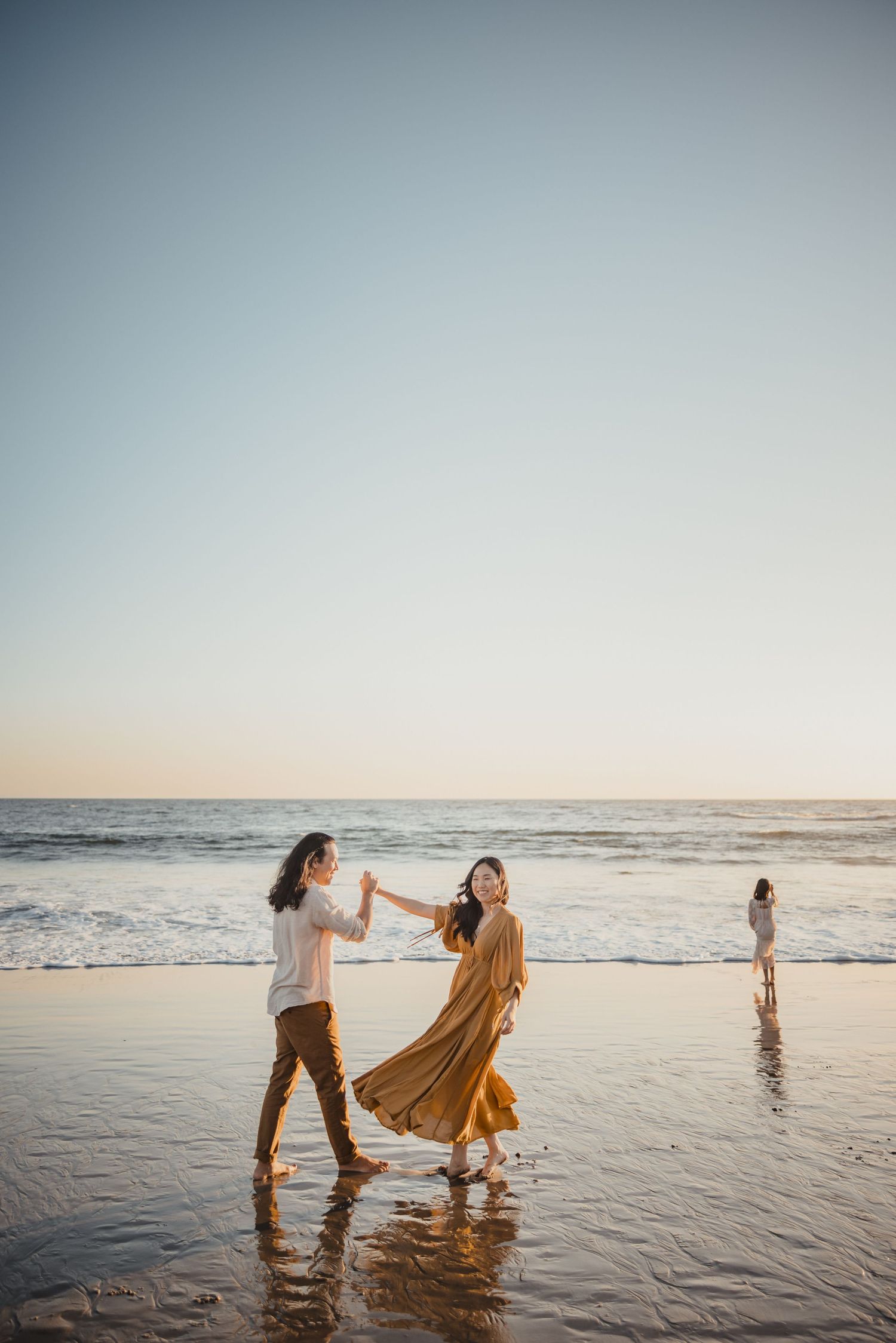 People dancing together at sunset on a scenic beach with waves and golden light reflecting off the wet sand.