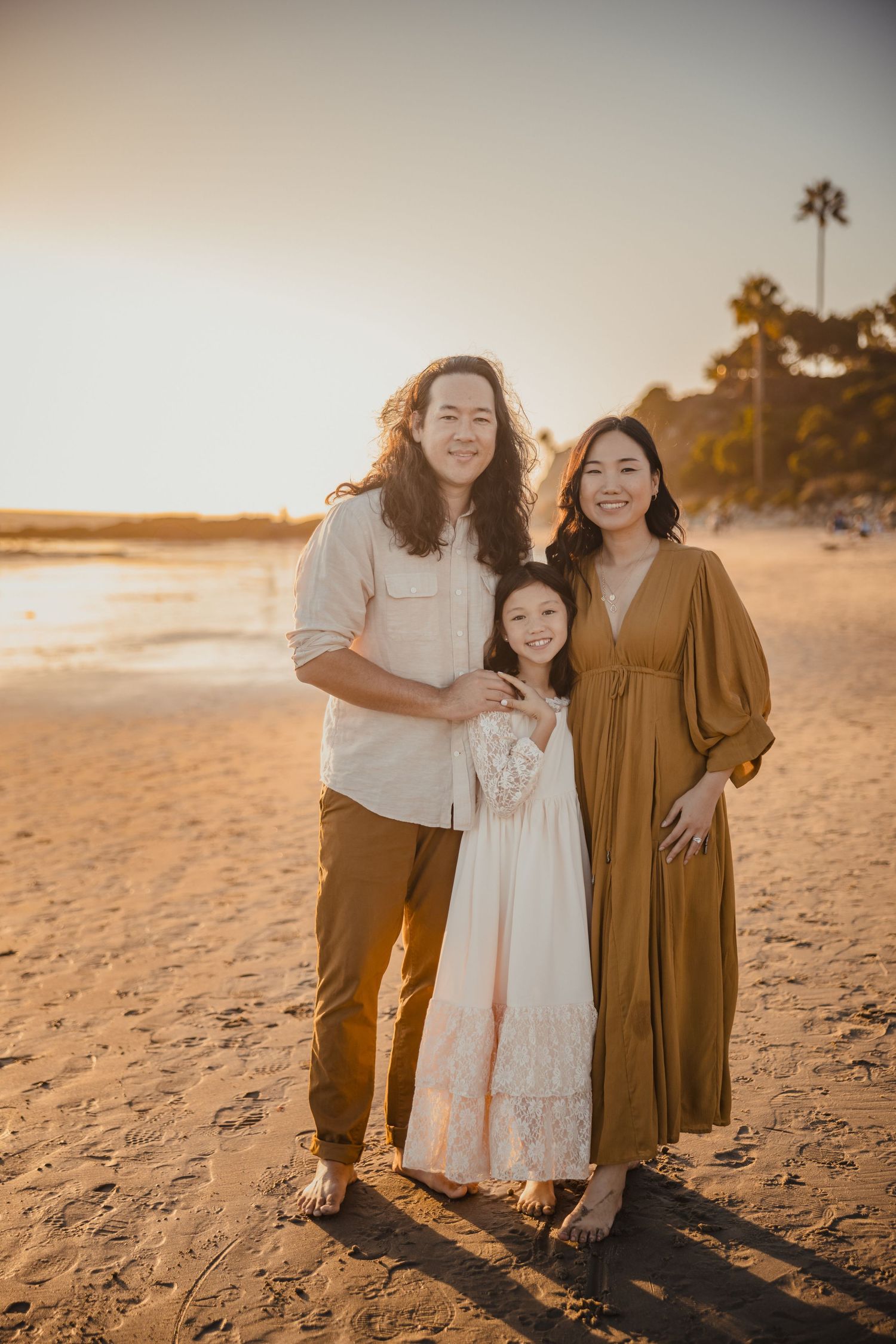 A family poses together on a golden sandy beach at sunset with palm trees in the background.