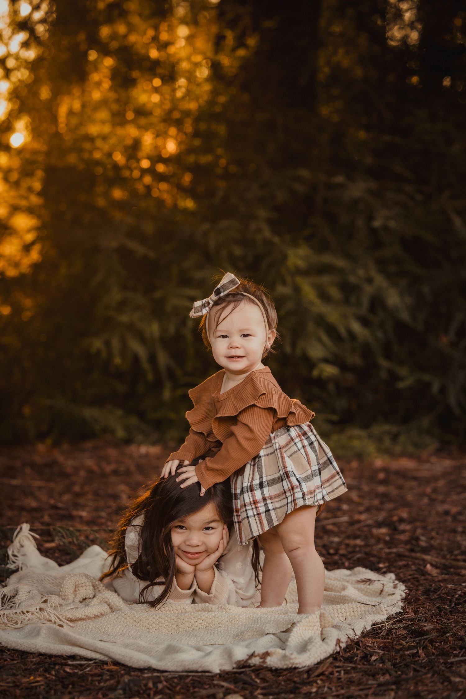 Two children playing together on a blanket in the woods at sunset with warm golden lighting.