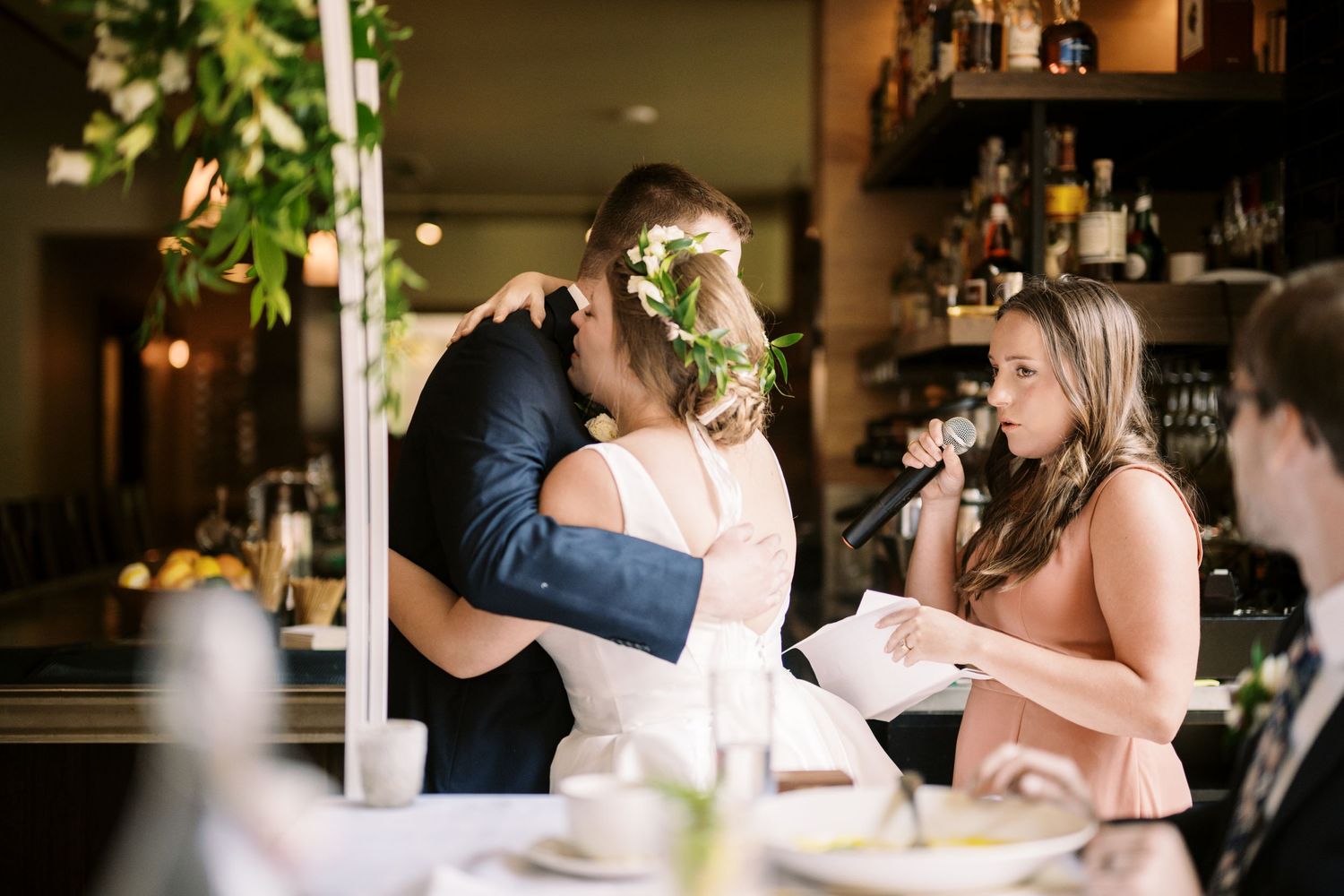A wedding celebration scene at a restaurant with people embracing and smiling while others nearby enjoy the moment.