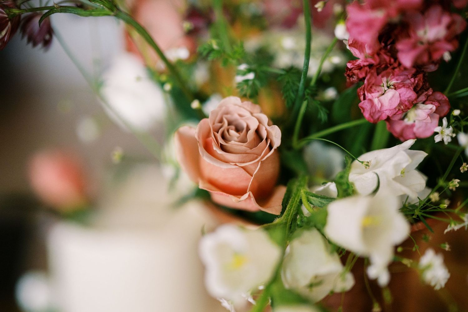 Soft peach rose and white bell-shaped flowers in a dreamy close-up bouquet with delicate greenery.