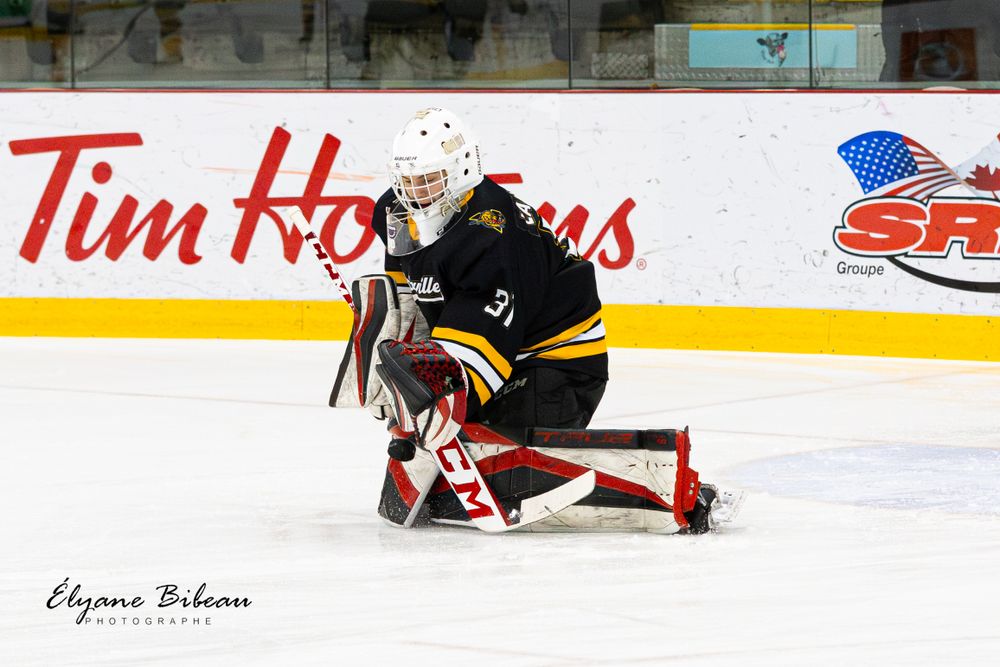 Goalie in dark uniform crouching in front of net with Tim Hortons advertisement visible.