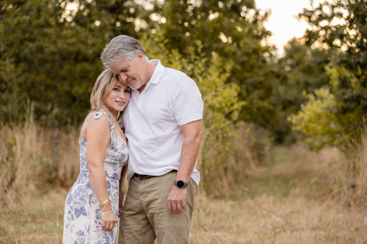 A romantic couple shares an intimate moment in a sunlit meadow during golden hour, wearing coordinated white and beige outfits.