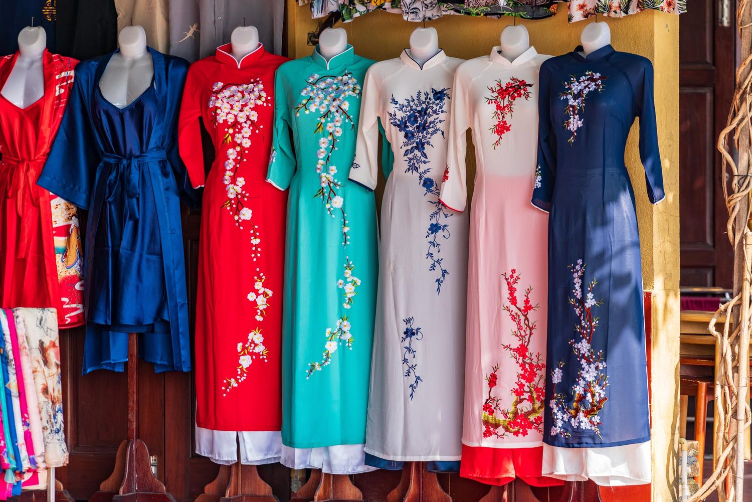 Colorful traditional Vietnamese ao dai dresses with floral embroidery hanging on display at a market stall. What should I buy in Hanoi must-
