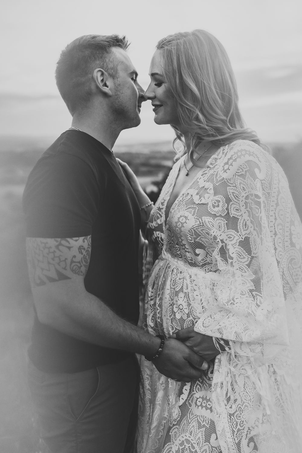 A couple shares an intimate moment in black and white, with her wearing a delicate lace dress against a dreamy background.