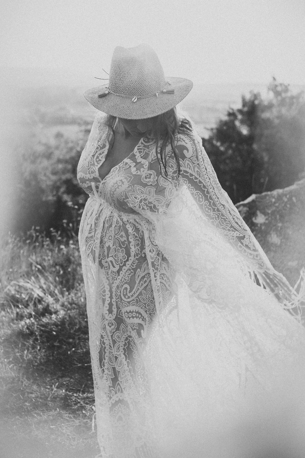 A dreamy black and white image of a person in a lace dress and cowboy hat standing in a misty field.