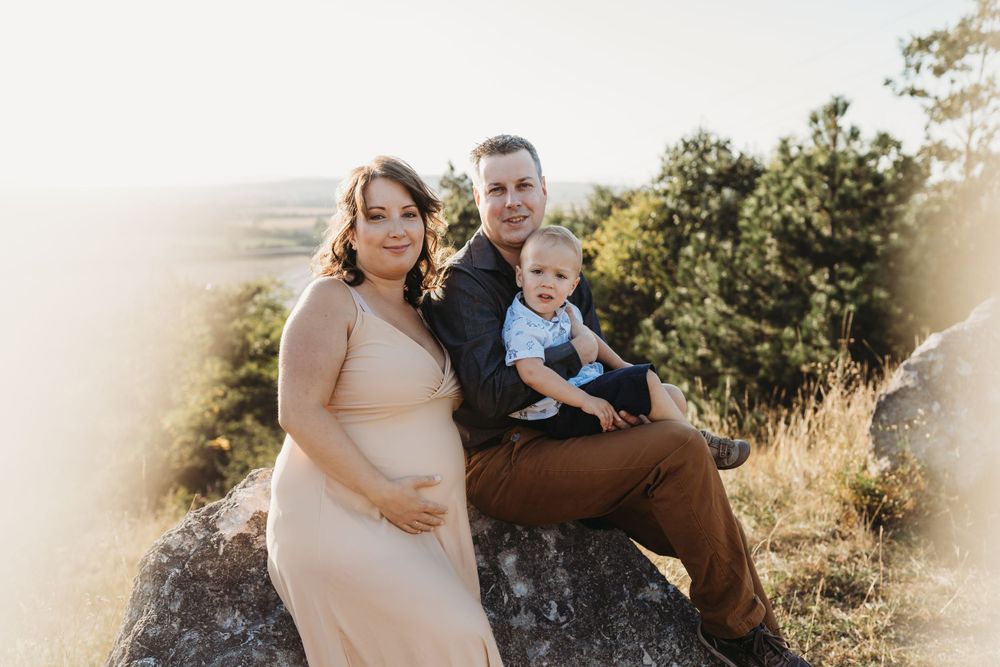 A family sits together on a rocky overlook during a sunset maternity photo session in nature.
