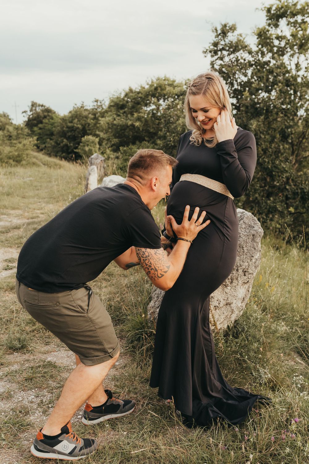A couple shares an intimate moment during a maternity photoshoot in a grassy outdoor setting.