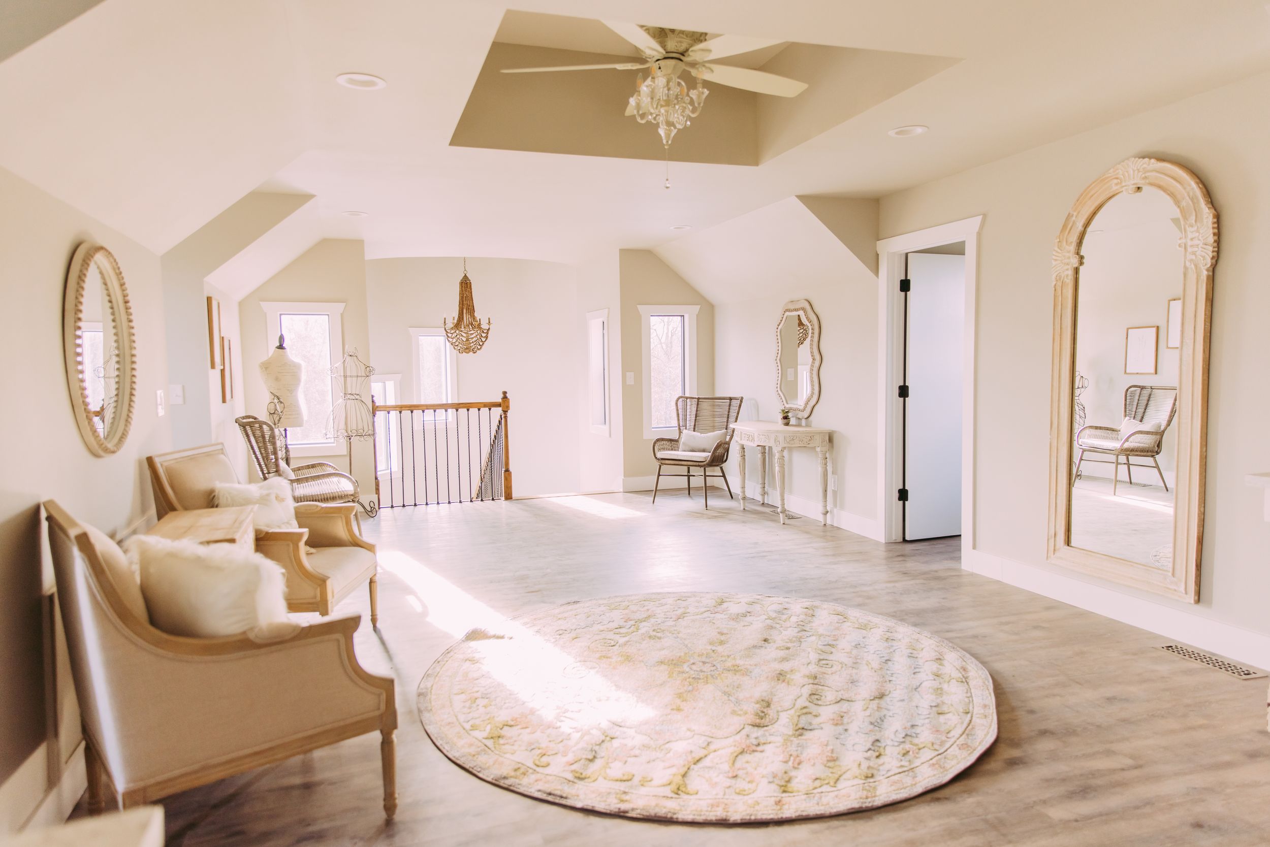 Elegant white master bedroom with oval mirrors, plush seating, and a round area rug in natural light.
