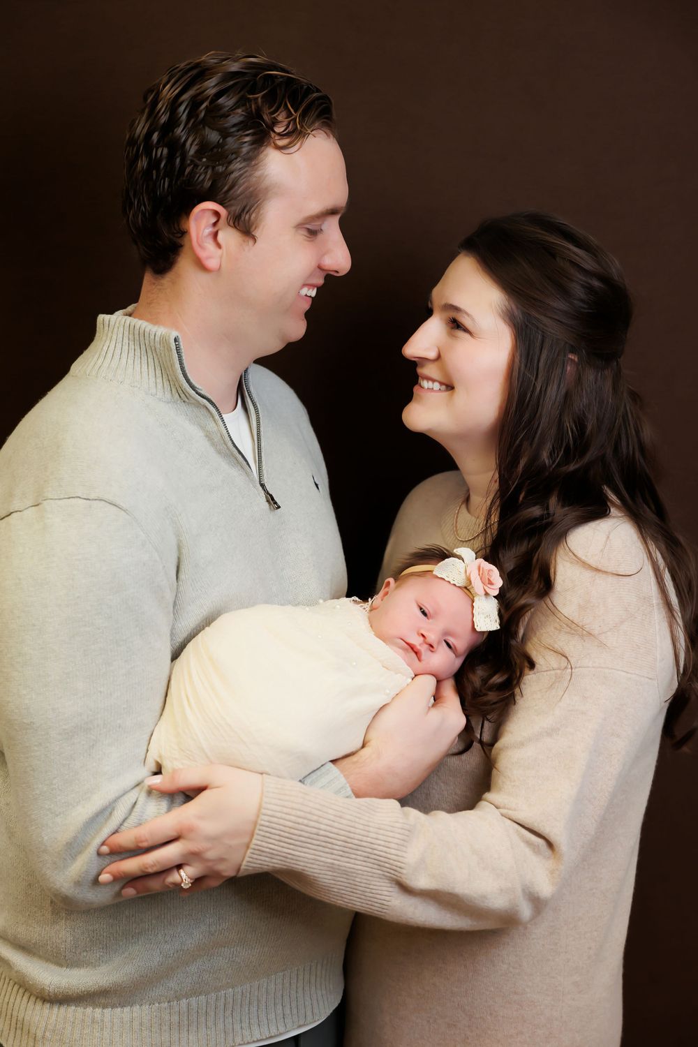 Sweet family moment with parents in neutral sweaters gazing at each other while holding their baby.