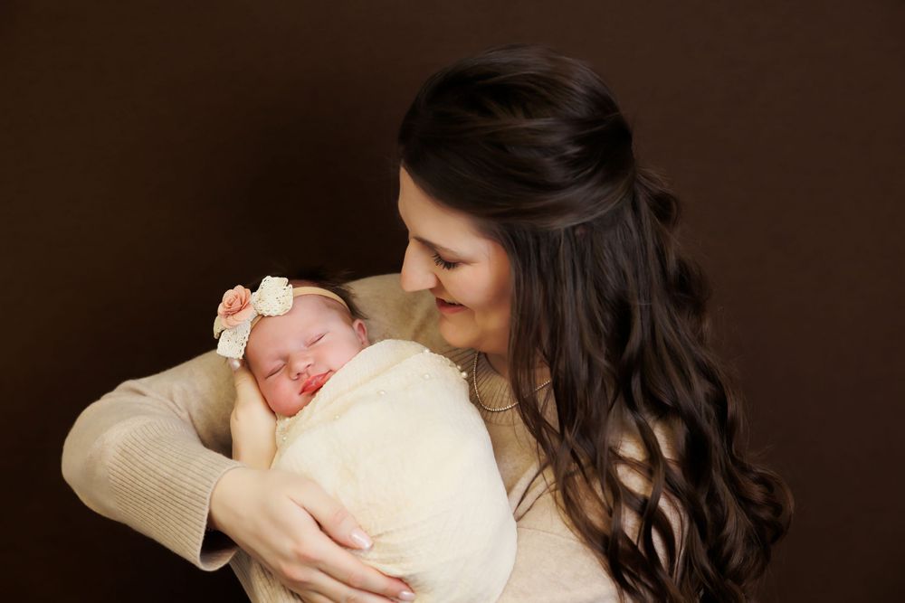 Tender moment between parent and sleeping newborn against dark background.