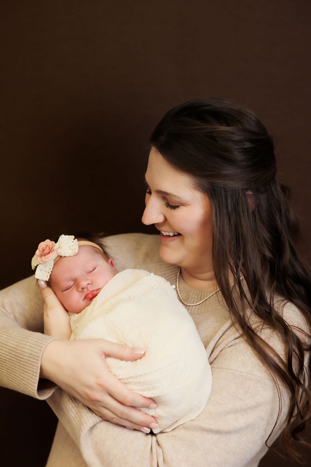 Sweet portrait of parent gazing lovingly at sleeping newborn in cream wrap.