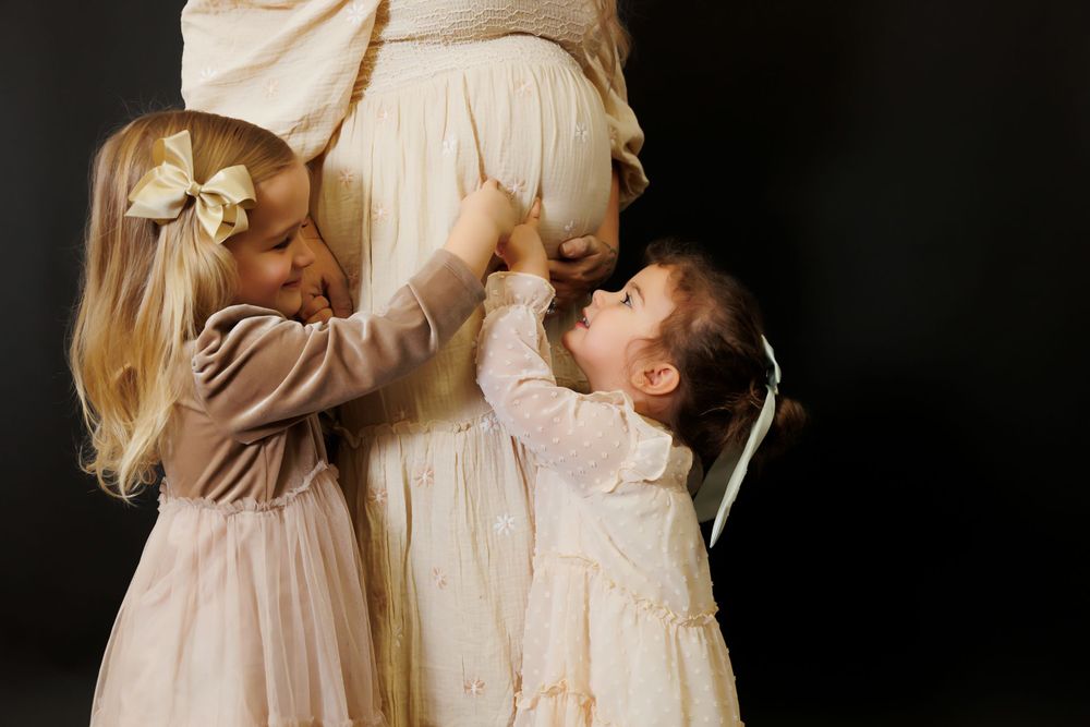 Two children in white dresses reach up together against a dark background.