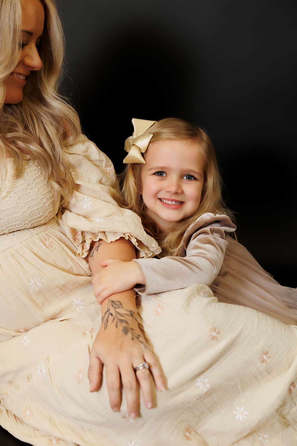 A heartwarming portrait of a mother in a cream dress and her young daughter with a bow sharing a tender moment.