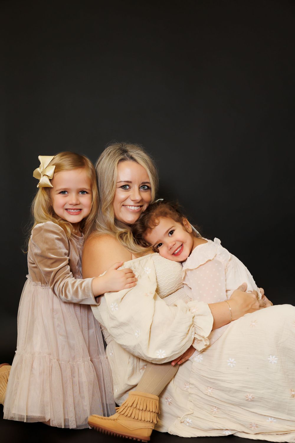 A family portrait with children wearing soft neutral colors against a dark background.